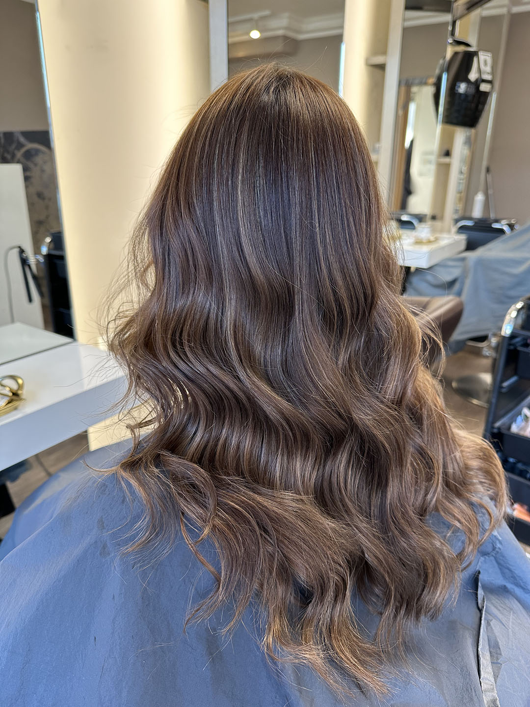 Langes, welliges braunes Haar mit sanften Locken, personenunbekannt, in einem Salonstuhl sitzend.