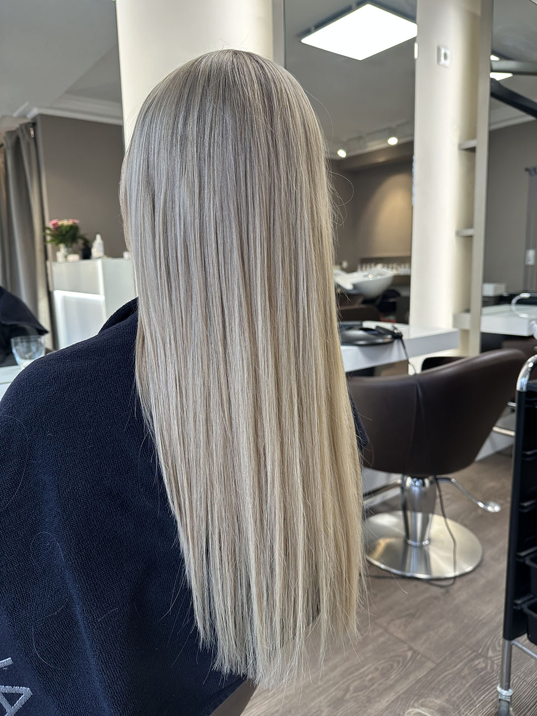 Lange blonde Haare, glatte Frisur im Friseursalon, Rückenansicht einer Person vor einem Spiegel.