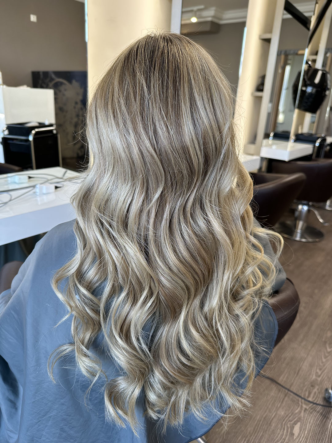 Langes, lockiges, blondes Haar einer Person im Friseursalon, Rückenansicht.